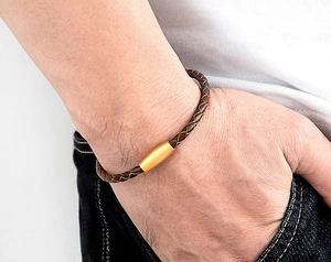Detail view of woven brown leather bracelet with matte gold magnetic clasp on a wrist