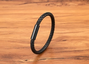Detail of black woven leather bracelet showing the matte black magnetic clasp on wood
