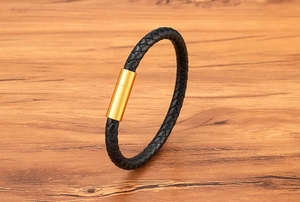 Detail of black braided leather bracelet with golden cylindrical magnetic stainless steel clasp