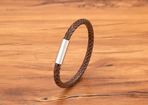 Detail of braided brown leather bracelet with silver magnetic cylinder clasp on wood