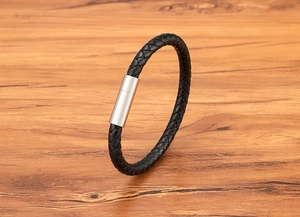 Detailed close-up of a black braided leather bracelet with a silver magnetic buckle on wood