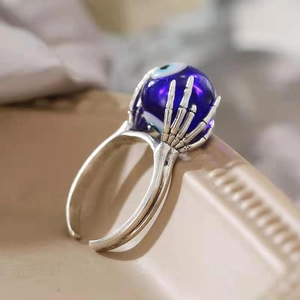 Makro-Detail des gotischen Evil-Eye-Rings mit Skeletthand auf einem Keramikständer