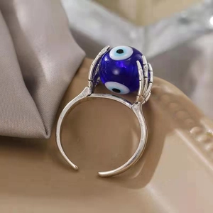Makroaufnahme einer silbernen Skeletthand mit blauem Teufelsauge auf einem Drehring