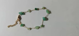 Detailed macro view of irregular green natural stone fragments on a gold chain bracelet
