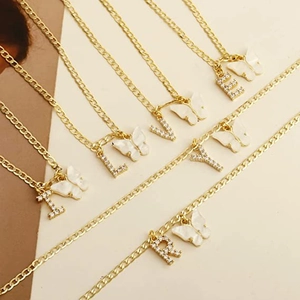 Detailansicht goldener Halsketten mit weißen Schmetterlingen und Buchstaben-Anhängern