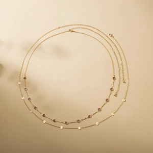 Detail view of double-layer gold chain with purple gemstones and round metal pendants