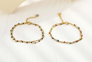 Dettaglio di bracciali a doppio strato dorati con perline colorate e ciondolo a cuore