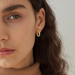 Nahaufnahme kleiner 18k Gold-Creolen, getragen mit einem warmen braunen Rollkragenpullover