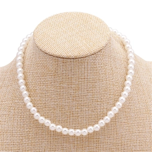 Élégant collier de perles blanches à un rang présenté sur un buste en lin de couleur beige