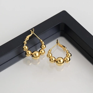 Gros plan de boucles d'oreilles boules dorées brillantes avec perles polies sur support