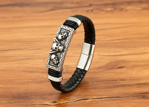 Detail of black woven leather men's bracelet with silver skull charm on wood surface