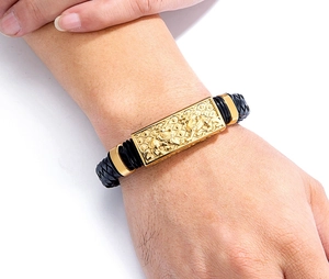 Detailansicht eines schwarzen Lederarmbands mit gravierter goldener Metallplatte