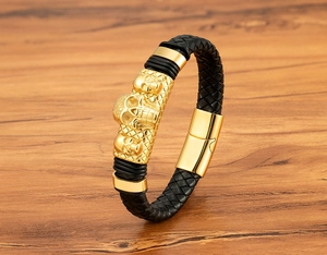 Detail of men's black braided leather bracelet featuring gold skull charms and magnetic clasp