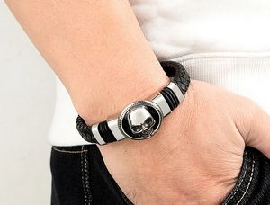 Dettaglio di un bracciale da uomo in pelle nera intrecciata con teschio d'argento al polso