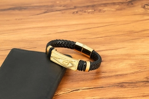 Détail d'un bracelet pour homme en cuir tressé noir avec charmes dorés sur bois