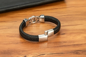 Close-up of black braided leather men's bracelet with vintage silver link on wood table