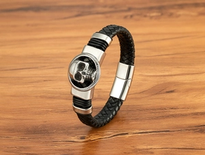 Dettaglio del charm a teschio argento su un bracciale in pelle intrecciata nera da uomo