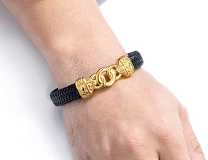Close-up of black braided leather bracelet with gold-tone metal links on a male wrist
