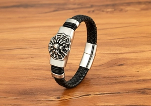 Détail d'un bracelet en cuir tressé noir avec fermoir araignée en argent vieilli sur bois