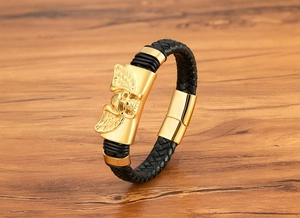 Dettaglio del teschio alato dorato su bracciale in pelle intrecciata nera da uomo