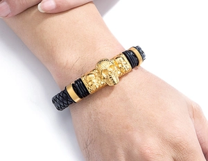 Detail of men's black braided leather bracelet featuring three golden skull metal charms