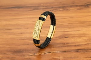 Détail bracelet en cuir tressé noir avec symbole maçonnique G doré et fermoir aimanté