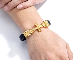 Nahaufnahme des goldenen Kruzifixes auf schwarzem Lederarmband mit Magnetverschluss