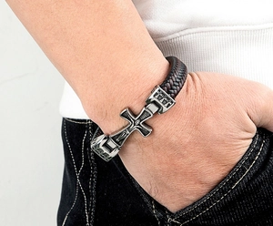 Detailansicht eines dunkelbraunen Lederarmbands mit geprägtem Kreuzanhänger aus Metall