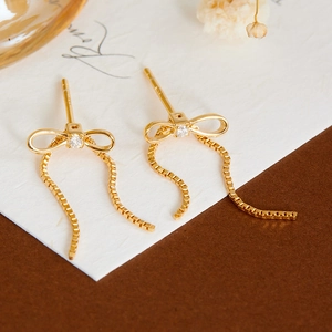Detail van vergulde zilveren strik oorbellen met moissanite en lange box ketting kwastjes