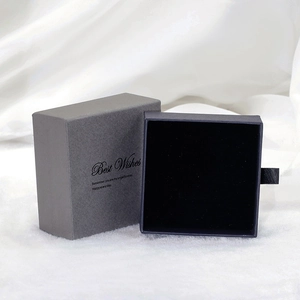 Détail d'un coffret à bijoux tiroir gris et noir avec texte doré posé sur de la soie