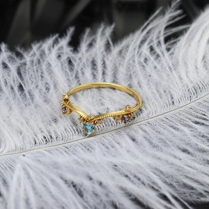 Macro detail van V-vormige gouden ring met blauwe hartsteen en paarse edelstenen op veer