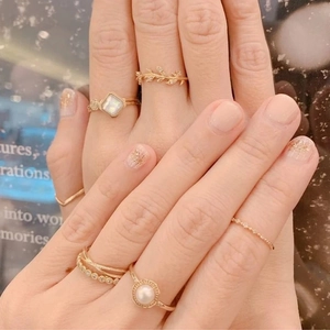 Nahaufnahme von goldenen Weizenblatt-Ringen und Perlen-Schmuckset an Frauenfingern
