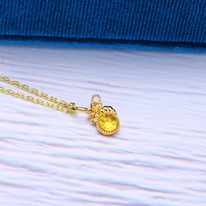 Close-up of golden bee necklace with round yellow amber stone on blue velvet backdrop