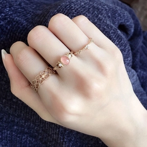 Dettaglio di tre anelli in oro rosa con una pietra rosa e motivo in pizzo