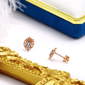 Detalle de pendientes de oro rosa con gema azul de corte marquesa y bordes de encaje