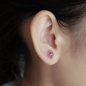 Detalle macro de pendientes de oro rosa con topacio azul marquise y encaje metálico