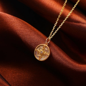 Makroaufnahme des goldenen Kleeblatt-Kompass-Anhängers mit Perlmutt und zentralem Diamanten