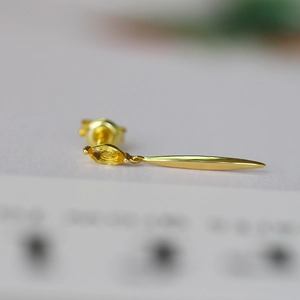 Macro shot of minimalist gold drop earring featuring a shuttle-shaped yellow gemstone