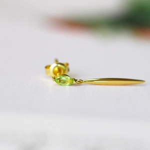 Macro shot of gold-plated leaf earring with marquise-cut olive green gemstone