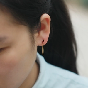 Close-up of leaf drop earrings in gold with red marquise stone on a female model