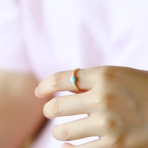 Close-up of a delicate gold ring featuring a blue larimar stone and zircon accents on a finger