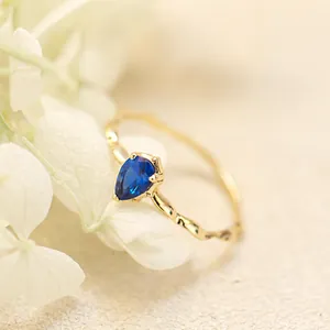 Primer plano de anillo dorado ondulado con espinela azul en forma de pera sobre una flor