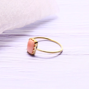 Détail d'une bague en nacre rose avec serti dentelé doré sur surface violette