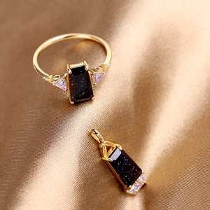 Détail d'un ensemble pendentif et bague en aventurine dorée sur du tissu de soie champagne