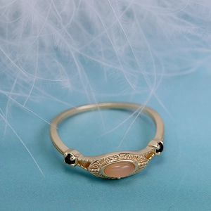 Vista macro de anillo vintage bañado en oro con piedra de luna rosa y detalles negros