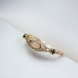Primer plano de anillo vintage dorado con piedra de luna rosa y diamantes negros