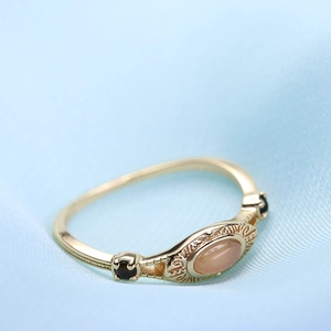 Vista macro de anillo vintage de oro con piedra luna naranja y gemas negras sobre seda