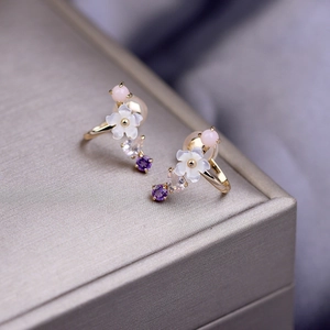 Detail of floral earring with natural shell petals and colorful gemstones in gold finish