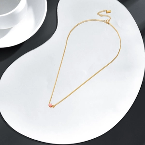 Dettaglio collana dorata con pendente in conchiglia rosa e perla bianca su base bianca