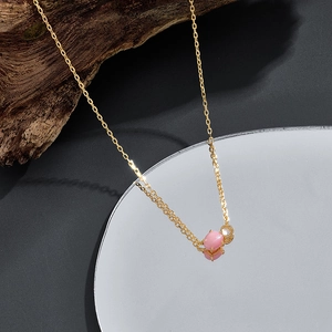 Dettaglio di una collana in argento placcato oro con ciondolo in conchiglia rosa su legno